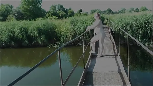 XXX Nostalgia do verão. Vestida de sol. Mulher nua sexy MILF caminha na ponte suspensa do rio. Nudistas. Naturistas. Praia de nudismo. Clipe erótico de música total de filmes